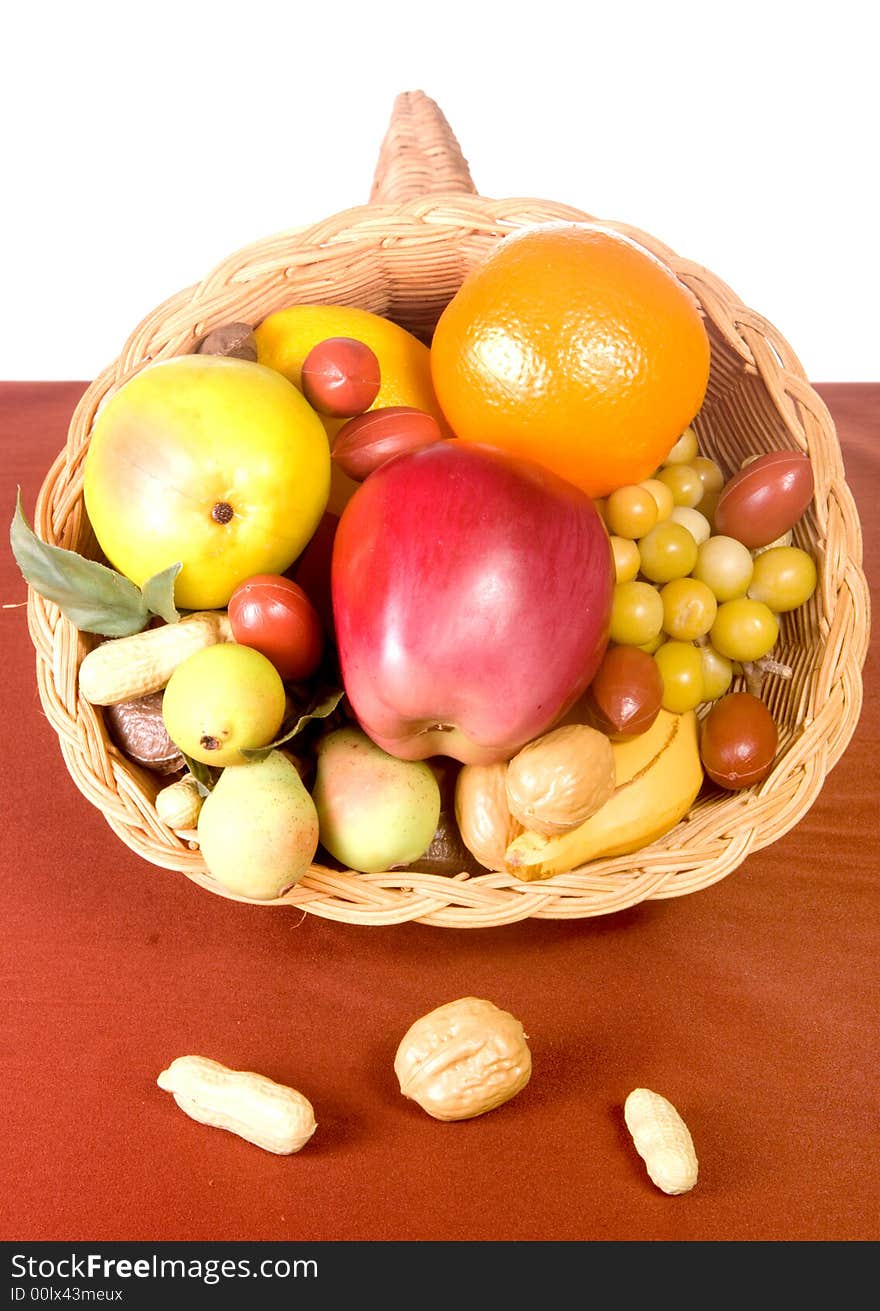 Wicker cornucopia filled with fruits and nuts on wicker placemat shot in studio over white