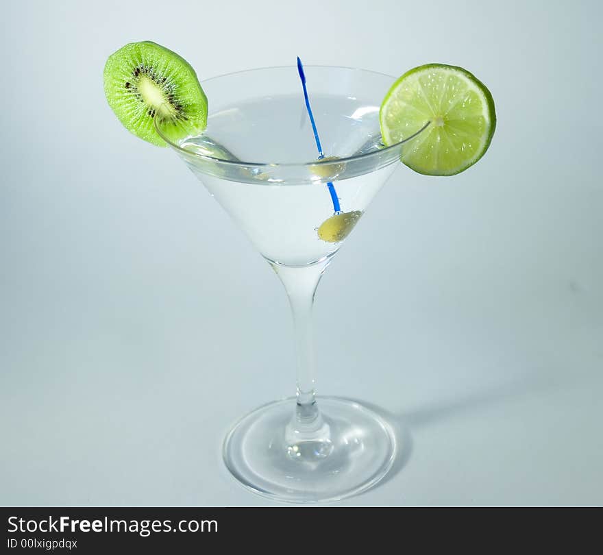 Martini glass with cocktail, green olive, lime and kiwifruit over white background. Martini glass with cocktail, green olive, lime and kiwifruit over white background