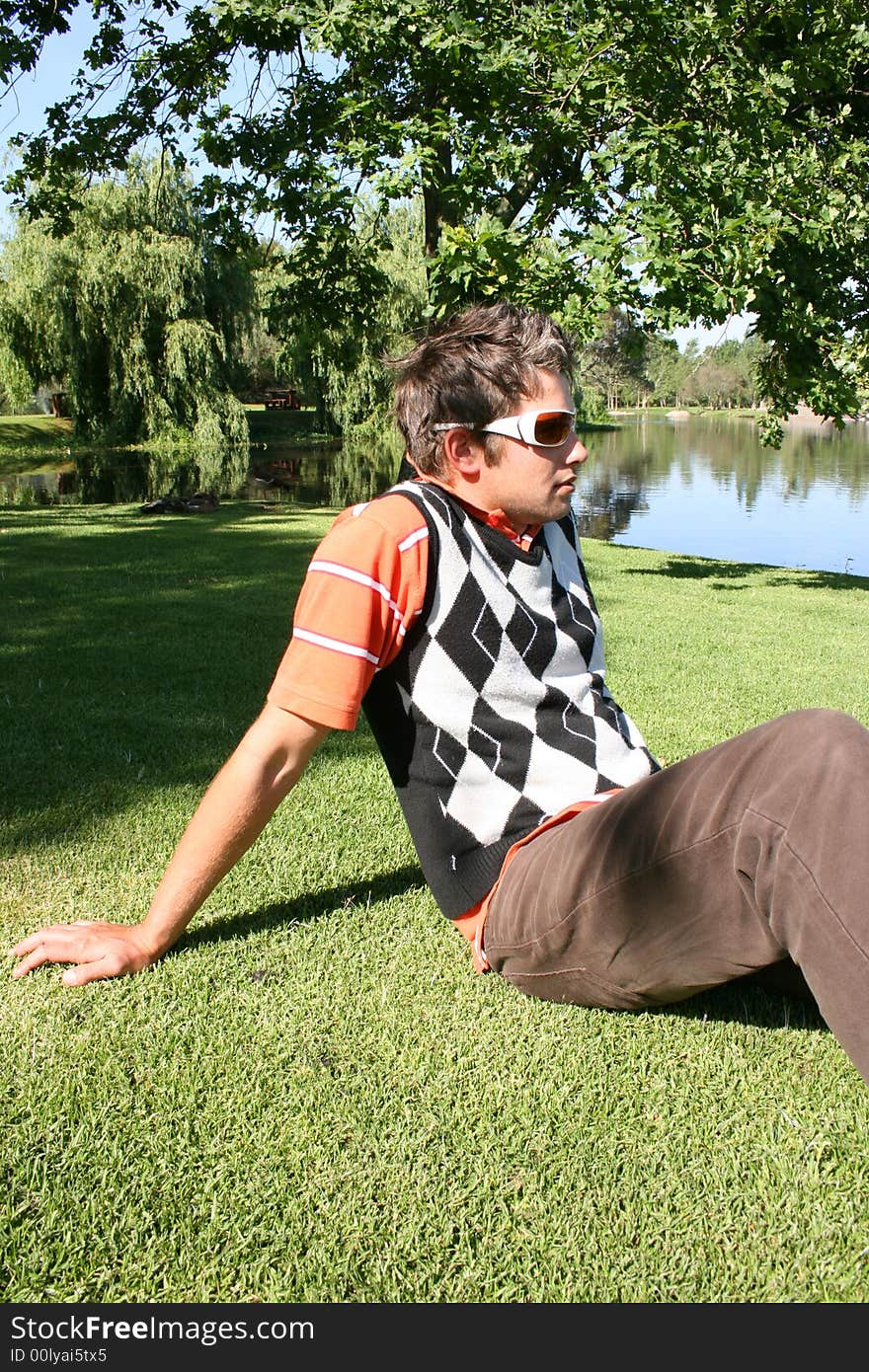 Young male model sitting in the park with water in the background. Young male model sitting in the park with water in the background