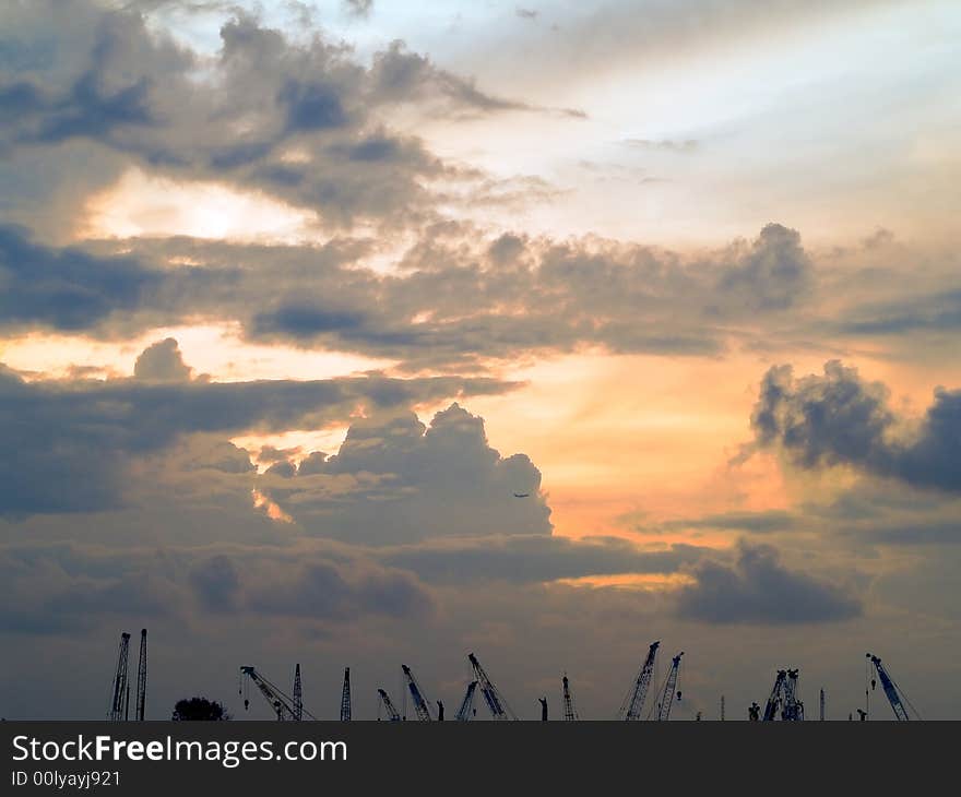 Cranes and an passenger aircraft silhouetted against stormy clouds as the sun breaks over the horizon. Cranes and an passenger aircraft silhouetted against stormy clouds as the sun breaks over the horizon.