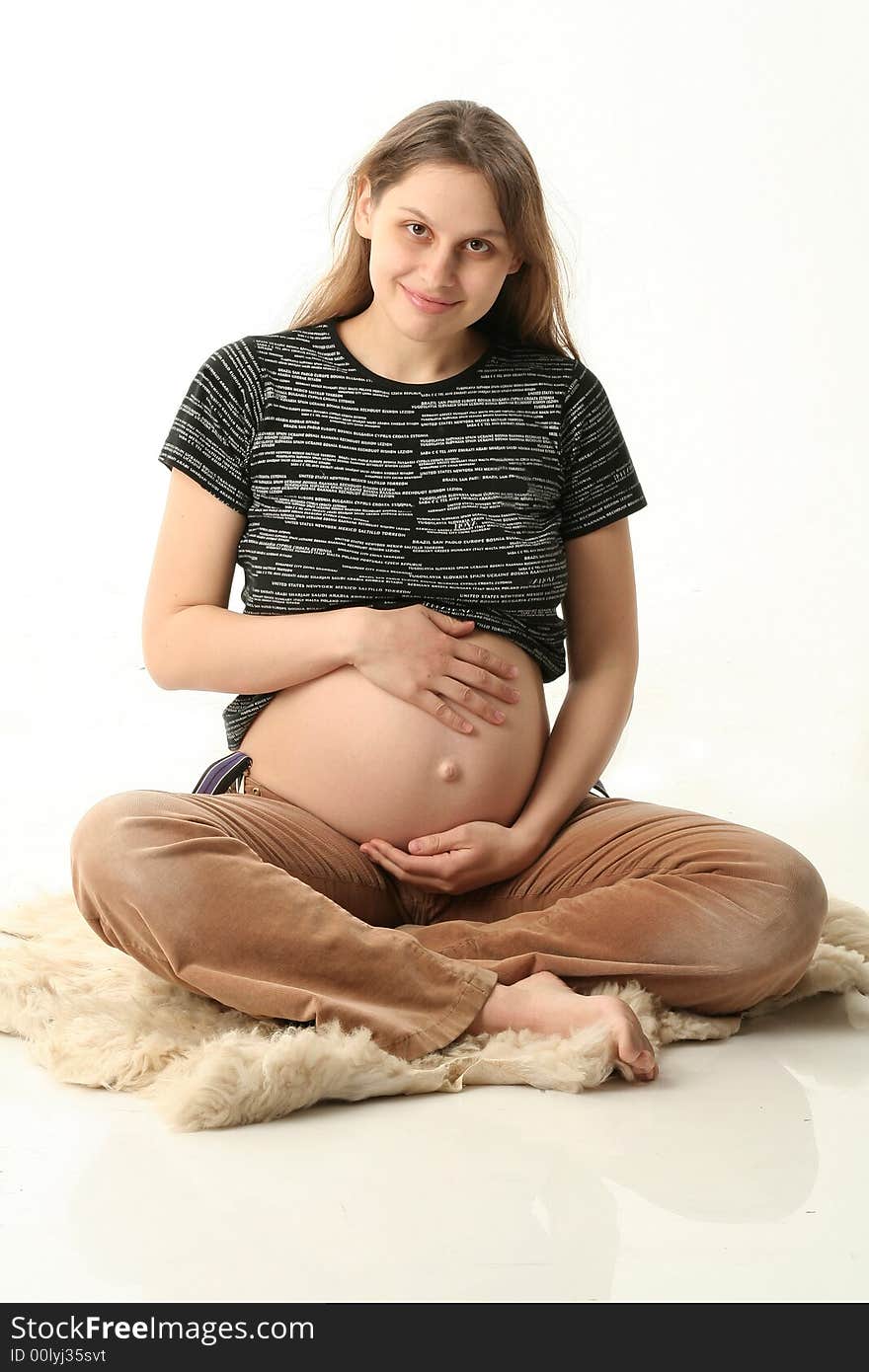 Happy young pregnant woman sitting on a floor and smiling. She is in black T-short , brown velvet pants. Happy young pregnant woman sitting on a floor and smiling. She is in black T-short , brown velvet pants