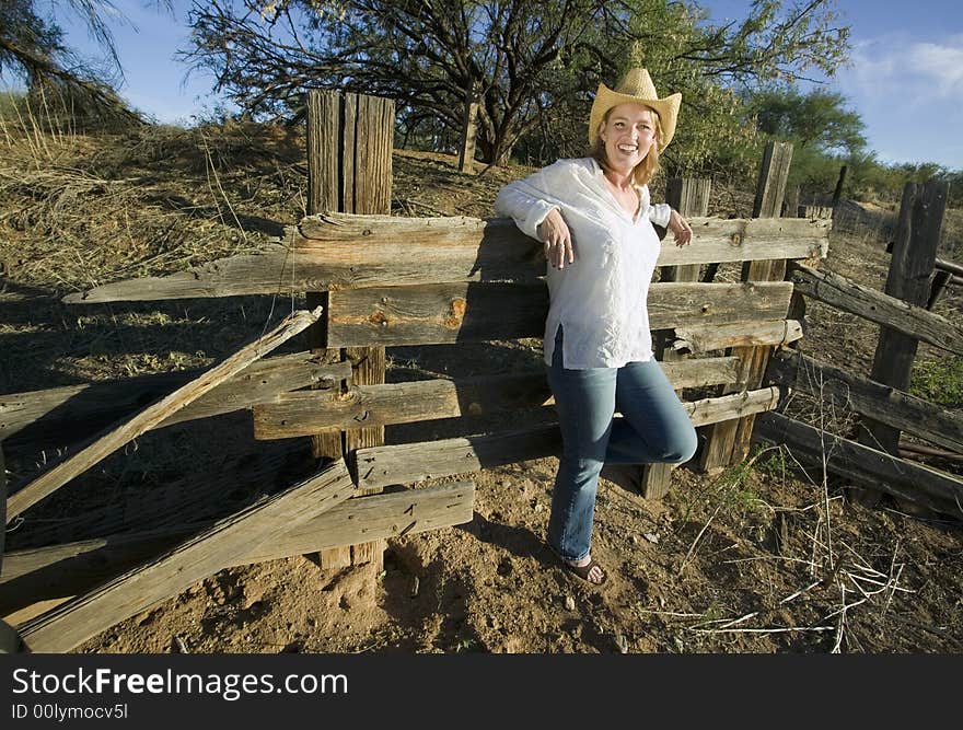 Western woman leans against a decrepit old split rail fence.