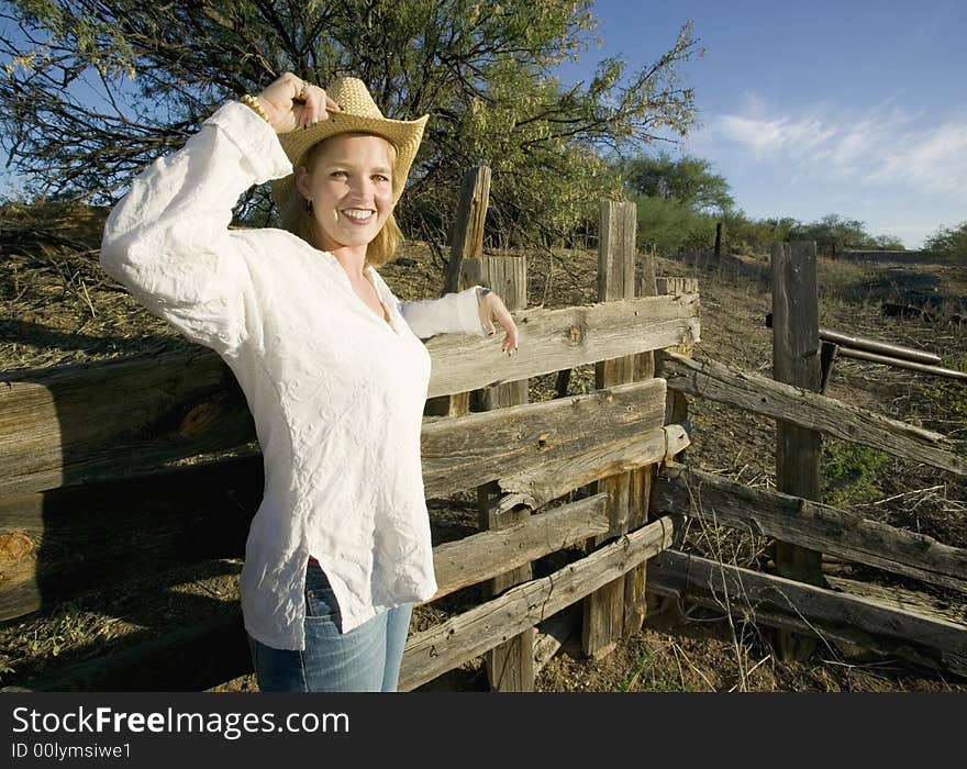 Western woman leans against a decrepit old split rail fence.