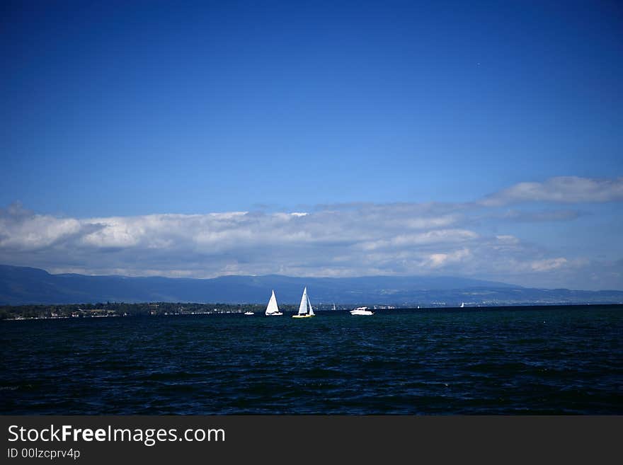 The sailboat at the far end of the picture and the blue sky and white clouds forms a beautiful picture. The sailboat at the far end of the picture and the blue sky and white clouds forms a beautiful picture.