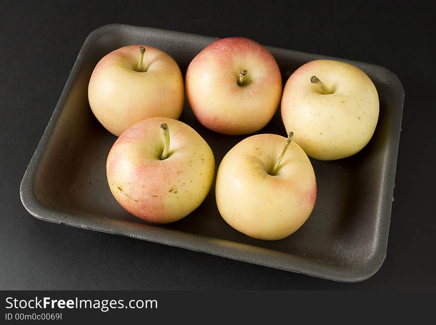 Apples in plastic tray over black background