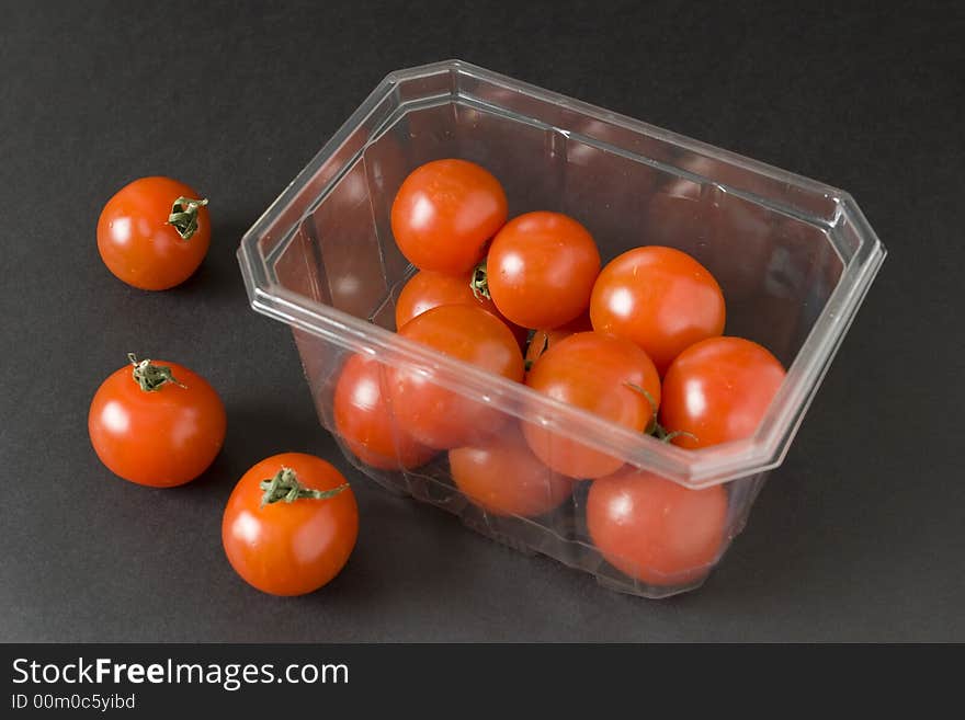 Cherry tomatoes in plastic container over black background. Cherry tomatoes in plastic container over black background