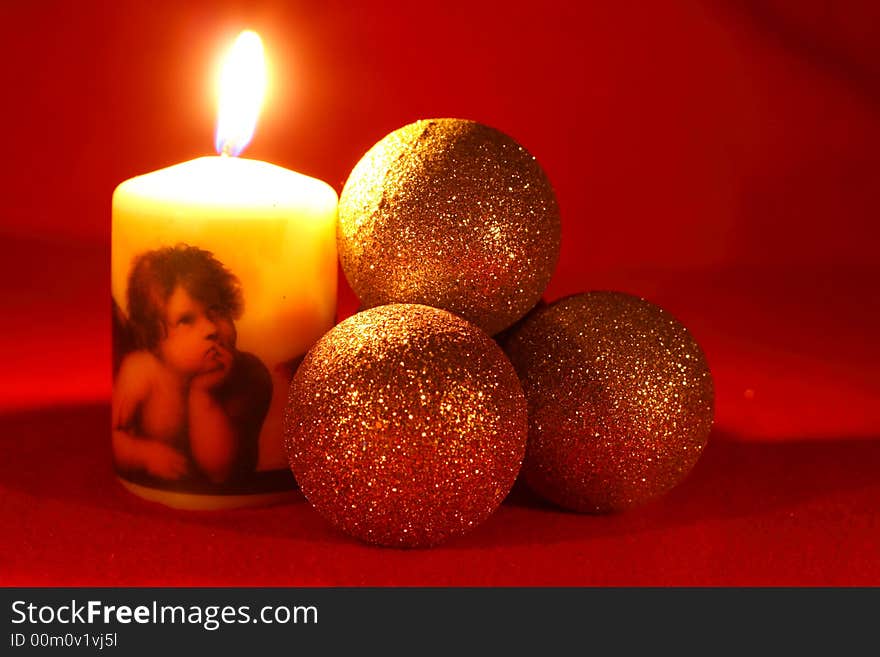 Candle with an angel and three christmas balls on a red background