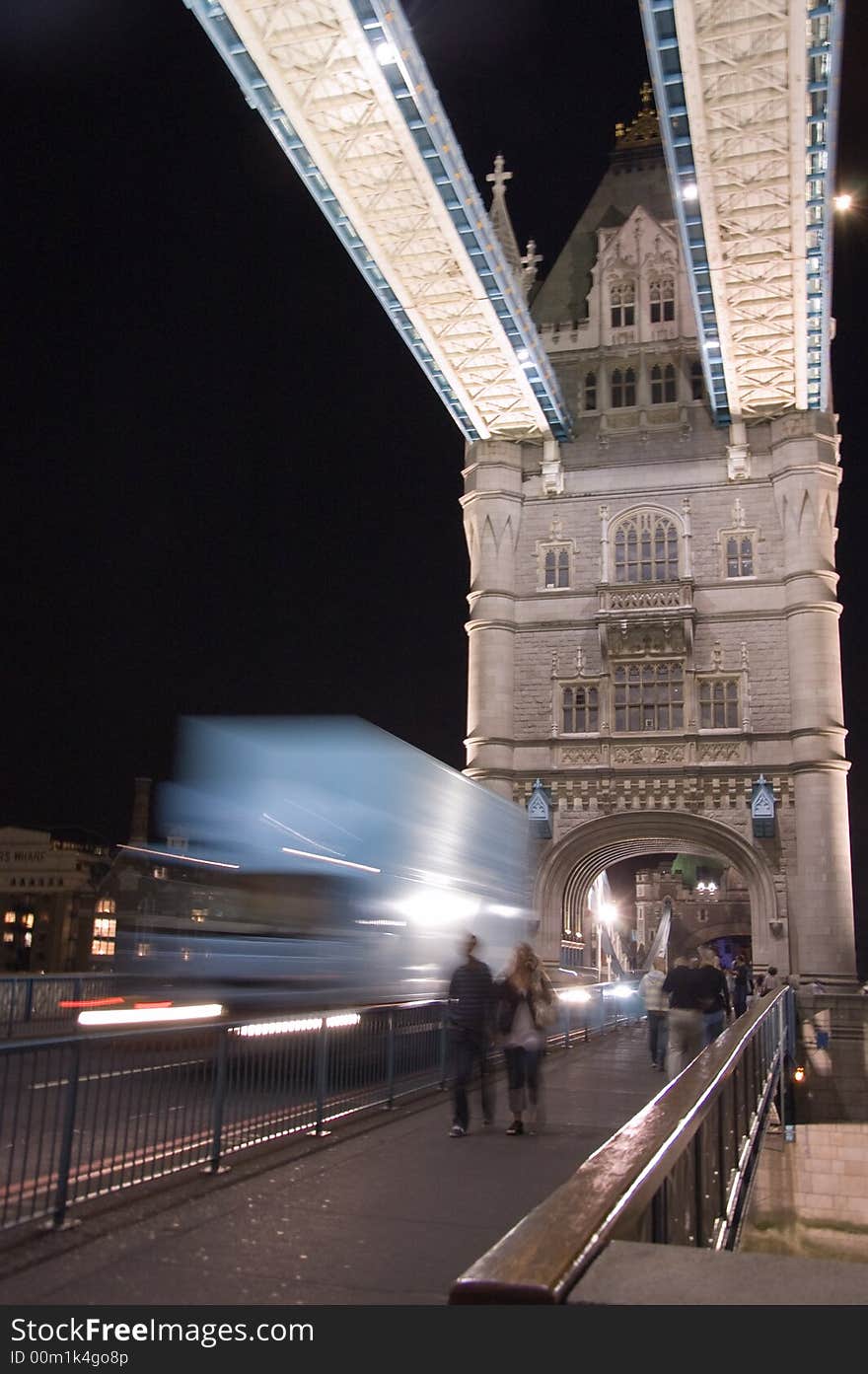 People walking and truck moving on Tower Bridge at night.