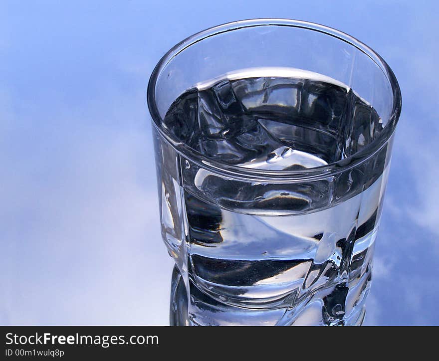 Glass of water on background with blue sky and clouds. Glass of water on background with blue sky and clouds