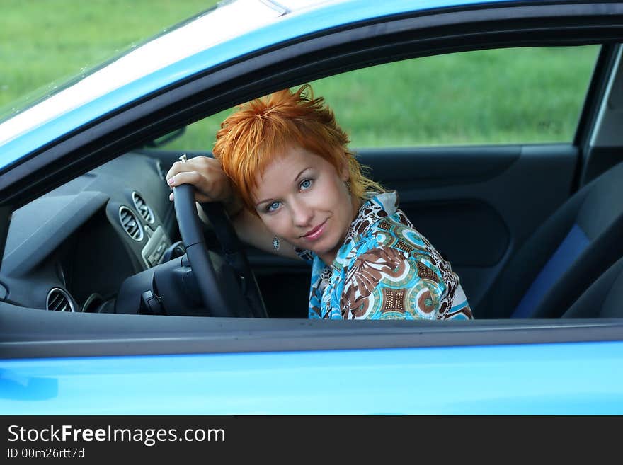 Young red-haired woman is siting in a car. Woman is happy