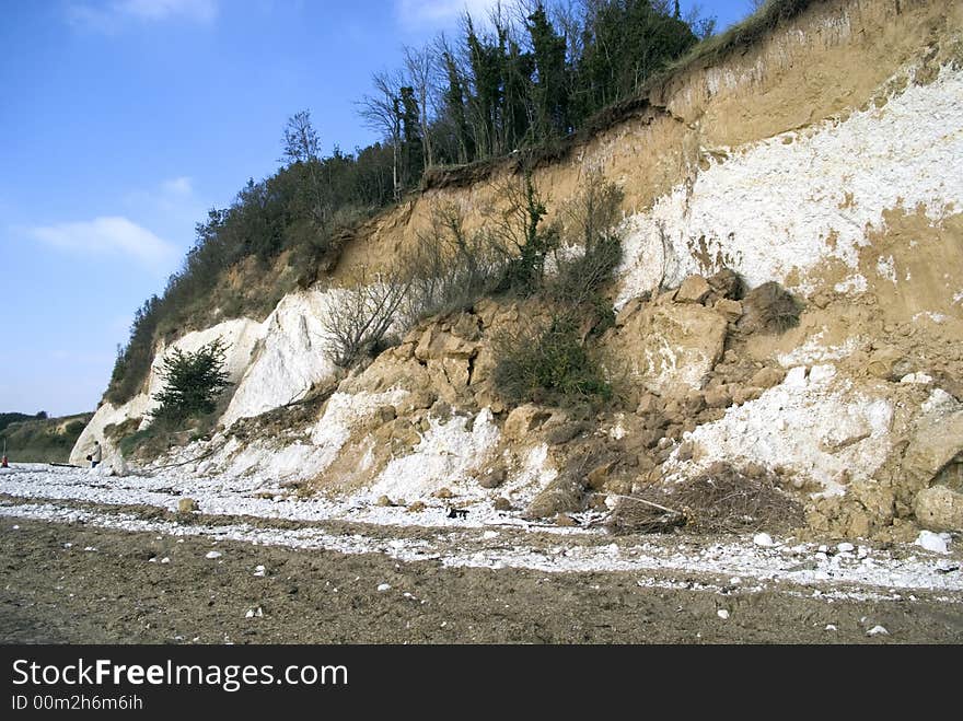 The falling cliff face with trees on the top, set against a blue sky. The falling cliff face with trees on the top, set against a blue sky