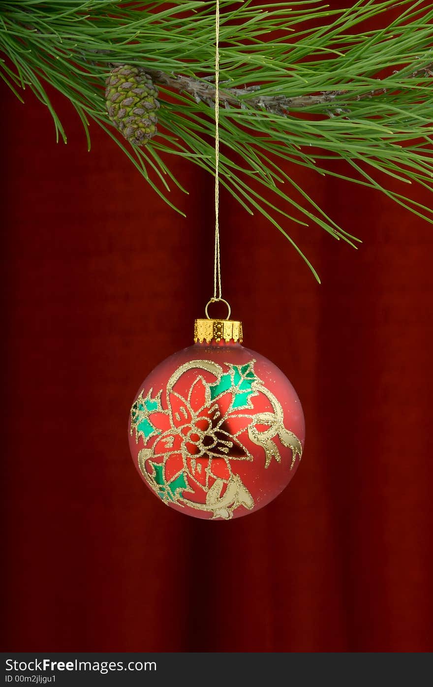 Christmas tree ornament with a pine tree branch in the top of the image, a red,gold and green holly decoration being the main focus. Christmas tree ornament with a pine tree branch in the top of the image, a red,gold and green holly decoration being the main focus