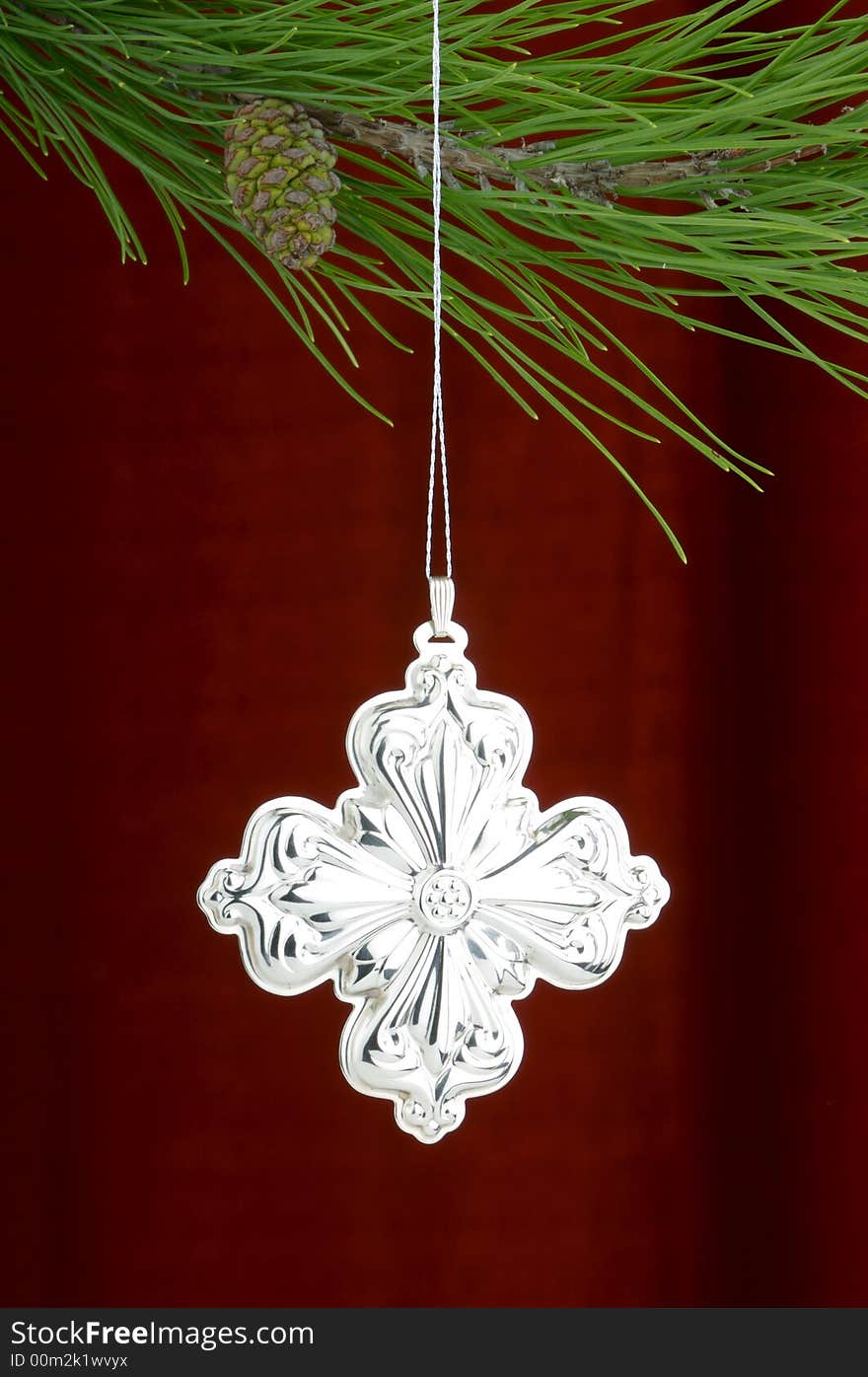 Christmas tree ornament with a pine tree branch in the top of the image, a silver cross decoration being the main focus. Christmas tree ornament with a pine tree branch in the top of the image, a silver cross decoration being the main focus