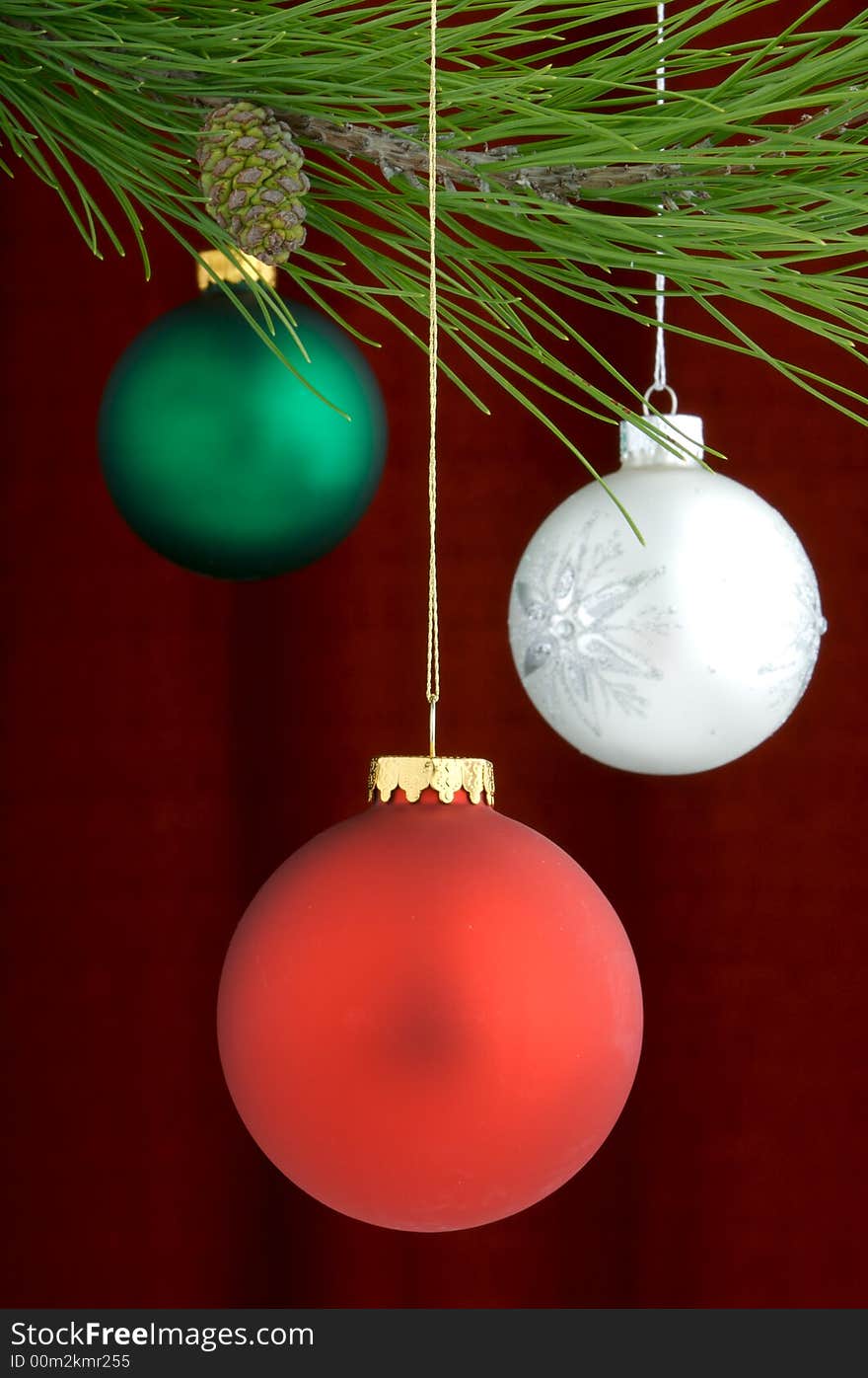 Three Christmas tree ornaments with a pine tree branch in the top of the image, a red decoration being the main focus. Three Christmas tree ornaments with a pine tree branch in the top of the image, a red decoration being the main focus