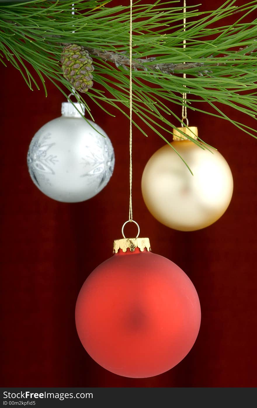 Three Christmas tree ornaments with a pine tree branch in the top of the image, a red decoration being the main focus. Three Christmas tree ornaments with a pine tree branch in the top of the image, a red decoration being the main focus