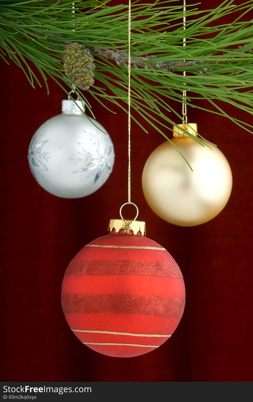 Three Christmas tree ornaments with a pine tree branch in the top of the image, a red, gold decoration being the main focus. Three Christmas tree ornaments with a pine tree branch in the top of the image, a red, gold decoration being the main focus