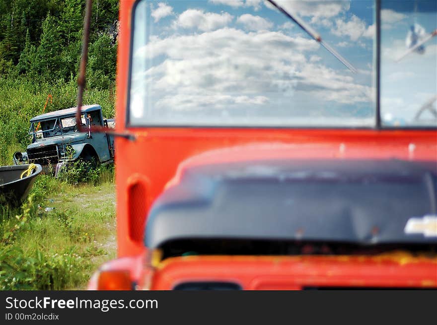 An abandoned bus sits out of focus in the foreground with fluffy clouds reflected perfectly in the windshield. in the background a broken down landrover sits in sharp focus. An abandoned bus sits out of focus in the foreground with fluffy clouds reflected perfectly in the windshield. in the background a broken down landrover sits in sharp focus.