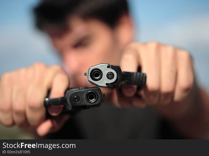 A young, robust man, in his 20's with dark hair pointing 2 pistols to the camera. A young, robust man, in his 20's with dark hair pointing 2 pistols to the camera.