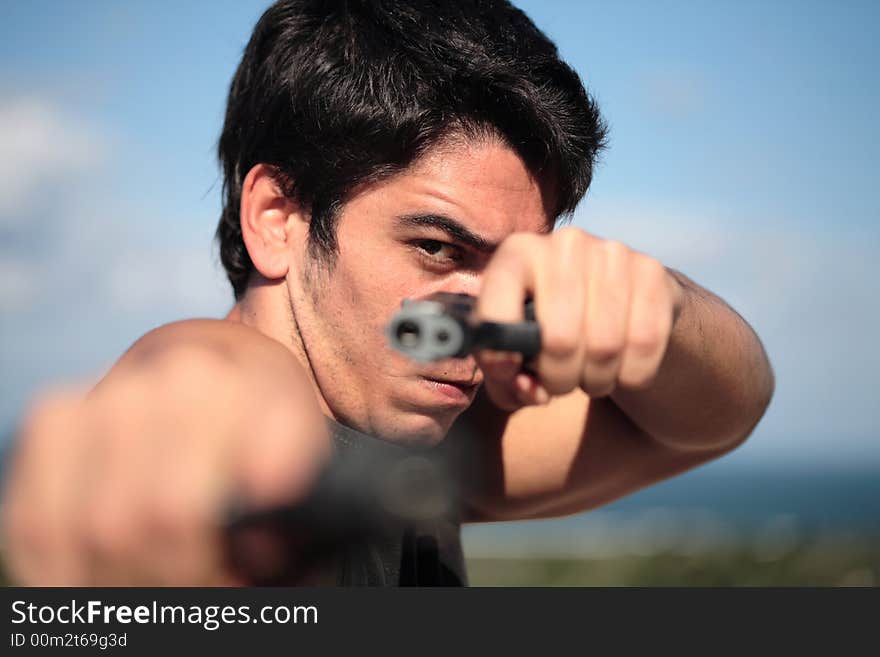 A young, robust man, in his 20's with dark hair pointing 2 pistols to the camera. A young, robust man, in his 20's with dark hair pointing 2 pistols to the camera.