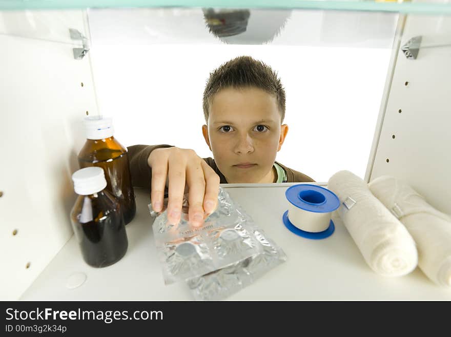 Young boy taking tablets from medicine chest. He's looking at camera. White background. Front view. Young boy taking tablets from medicine chest. He's looking at camera. White background. Front view