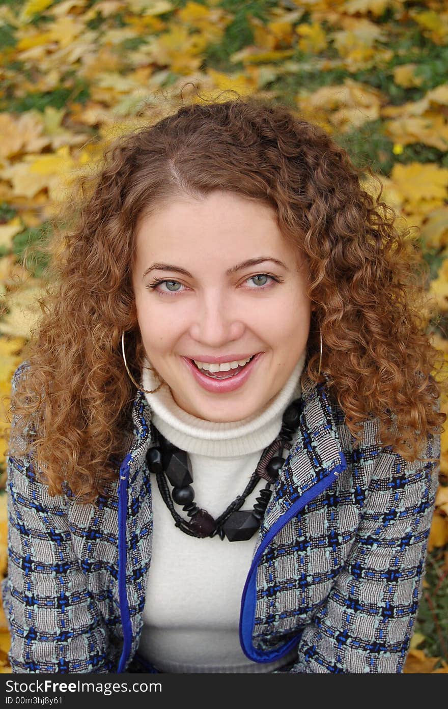 Beautiful positive girl with curling hair smiling to the autumn at the landscape covered by yellow leaves