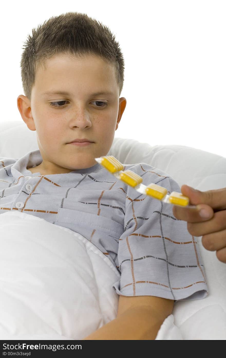 Young boy looking at yellow tablets. He's lying in the bed. White background. Young boy looking at yellow tablets. He's lying in the bed. White background