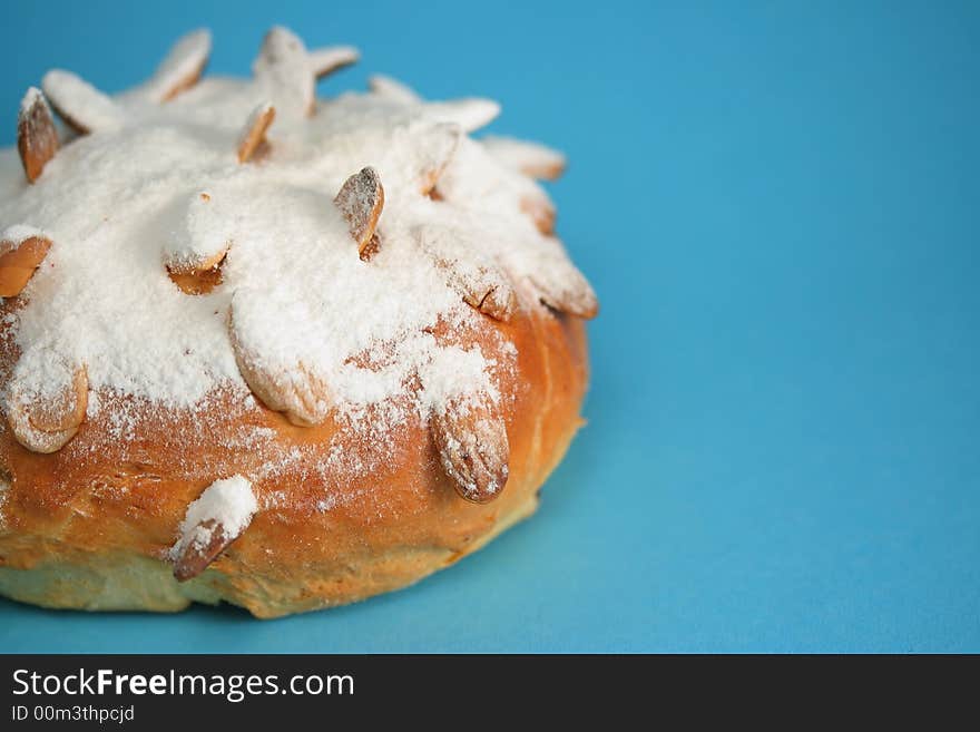 A detail of an Easter bun (fancy bread) with roast almonds and a lot of sugar on it; blue background. A detail of an Easter bun (fancy bread) with roast almonds and a lot of sugar on it; blue background.