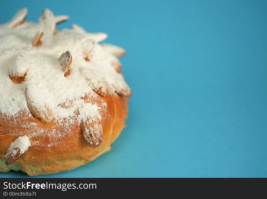 A detail of an Easter bun (fancy bread) with roast almonds and a lot of sugar on it; blue background. A detail of an Easter bun (fancy bread) with roast almonds and a lot of sugar on it; blue background.