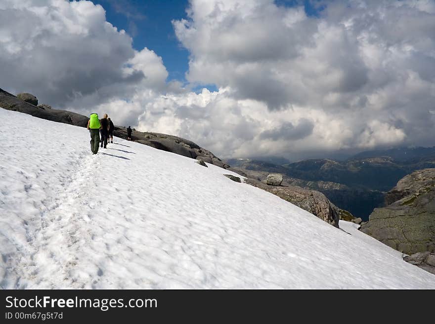 BASE-jumpers hiking by the trail through the snow field. Kjerag mountauns, Norway. BASE-jumpers hiking by the trail through the snow field. Kjerag mountauns, Norway.