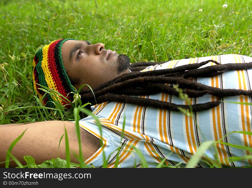 Sad Rastafarian Jamaican thinking laid on grass. Sad Rastafarian Jamaican thinking laid on grass