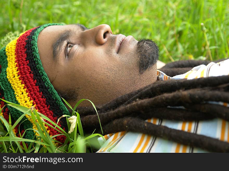 Sad Rastafarian Jamaican thinking laid on grass. Sad Rastafarian Jamaican thinking laid on grass