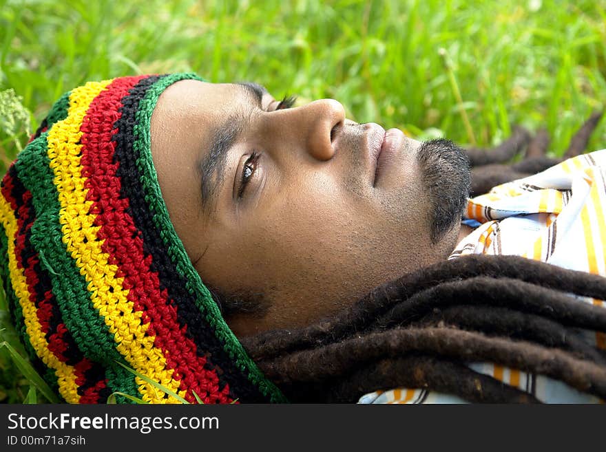 Sad Rastafarian Jamaican thinking laid on grass. Sad Rastafarian Jamaican thinking laid on grass