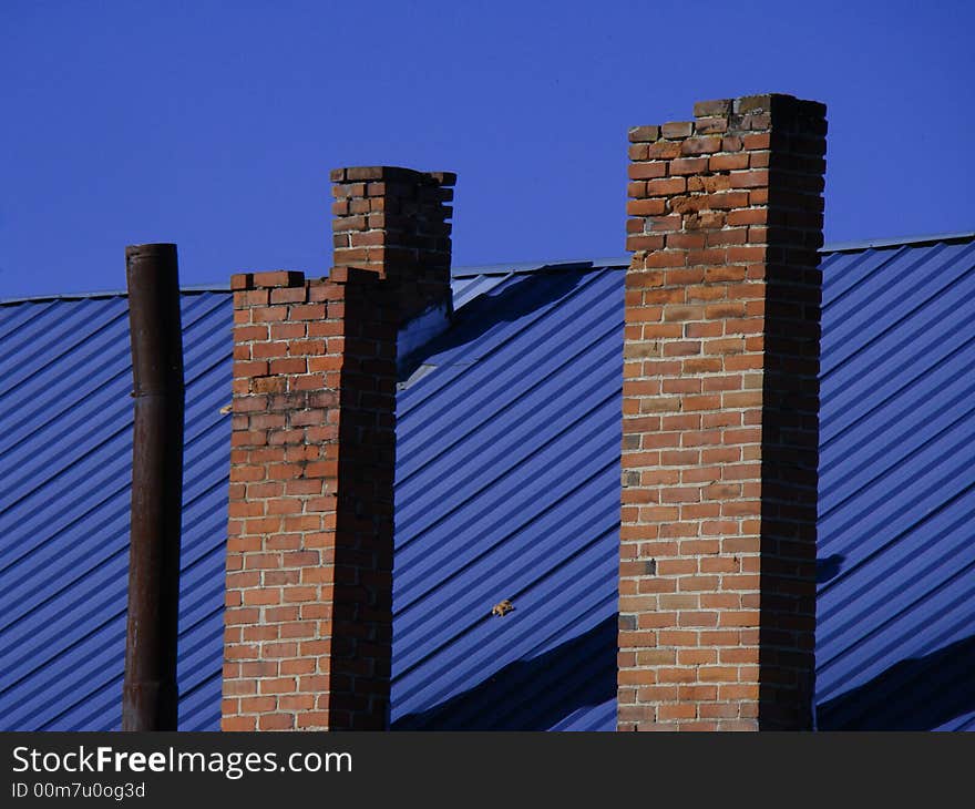 Four chimneys on a blue roof in front of a blue sky.