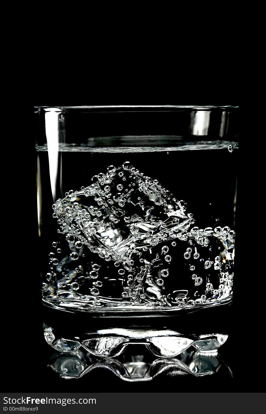 Ice cubes in glass of water with bubbles, isolated, black background