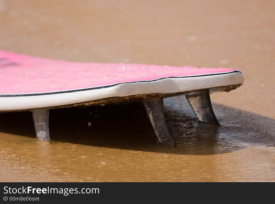 Pink surfboard washed up on the beach with fins stuck in the sand. Pink surfboard washed up on the beach with fins stuck in the sand