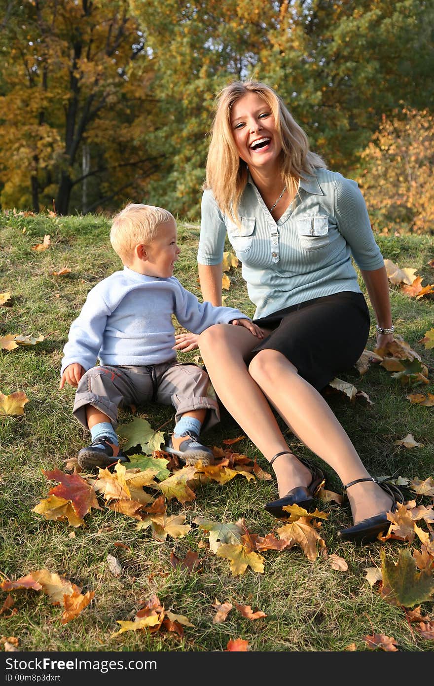 Blue-eyed blond sits with the son in the park in autumn. Blue-eyed blond sits with the son in the park in autumn