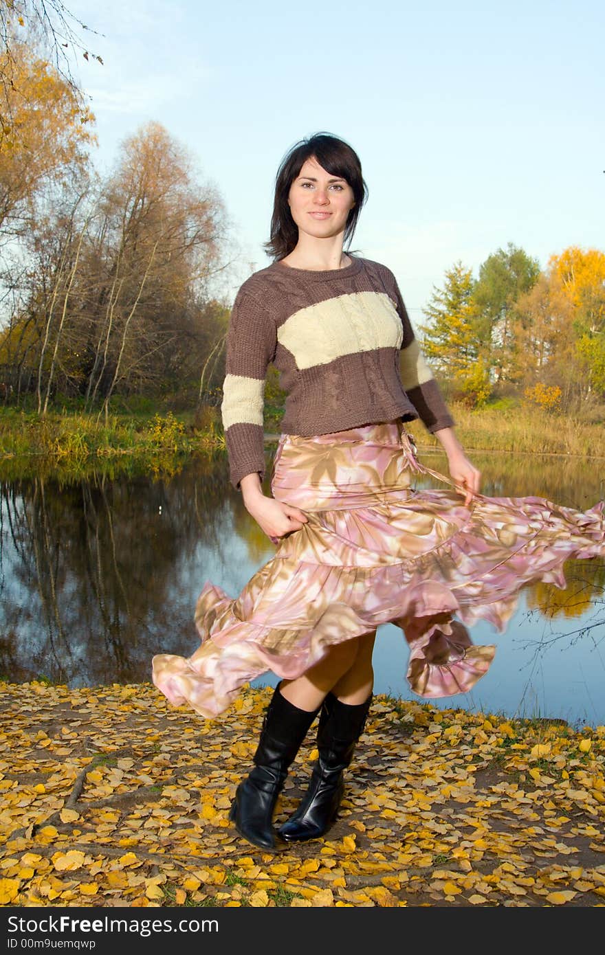 Young beautiful woman dancing at autumn park near small pond.