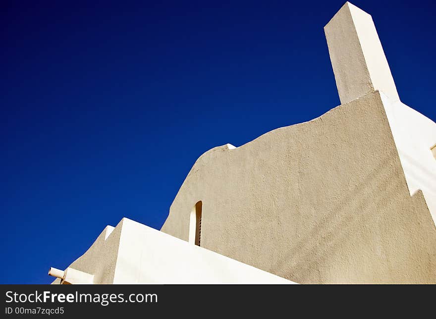 The angles, curves, and corners of the top of a building framed against a deep blue cloudless sky. The angles, curves, and corners of the top of a building framed against a deep blue cloudless sky.