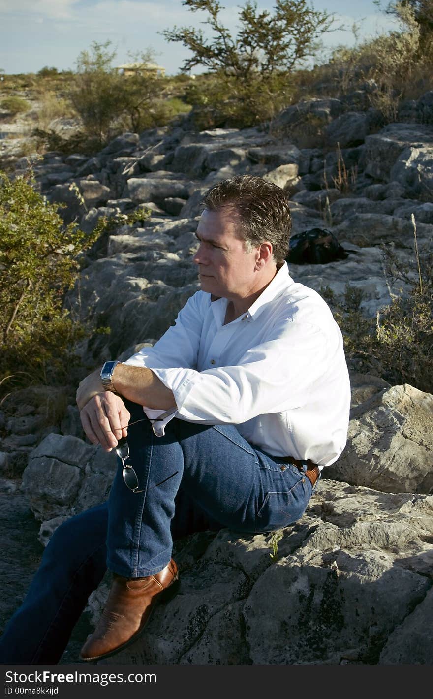 A man, leisurely enjoying the view from his perch on the side of a rocky hill. A man, leisurely enjoying the view from his perch on the side of a rocky hill.