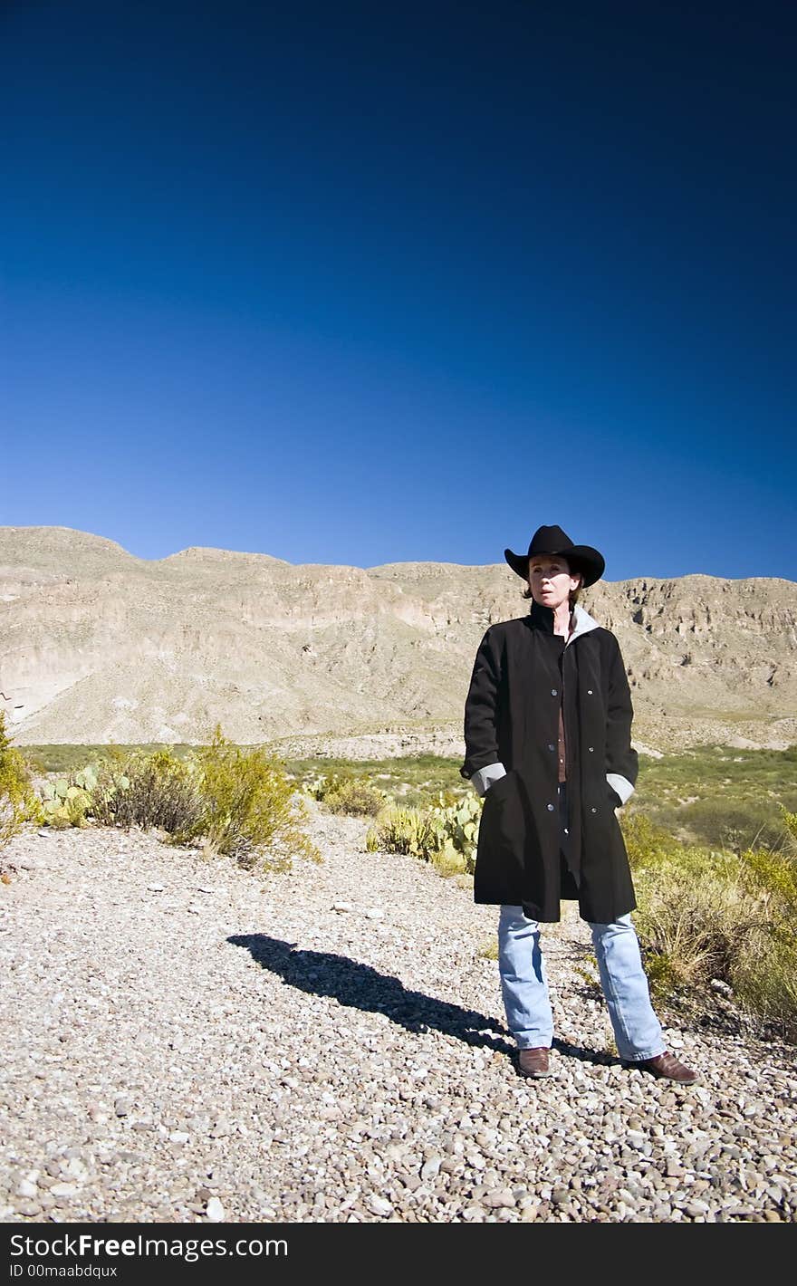 A woman dressed in a black coat and black western hat observing her surroundings. A woman dressed in a black coat and black western hat observing her surroundings.