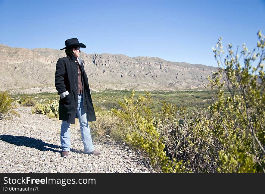 A woman dressed in western attire looking out at the rugged terrain layed out before her. A woman dressed in western attire looking out at the rugged terrain layed out before her.