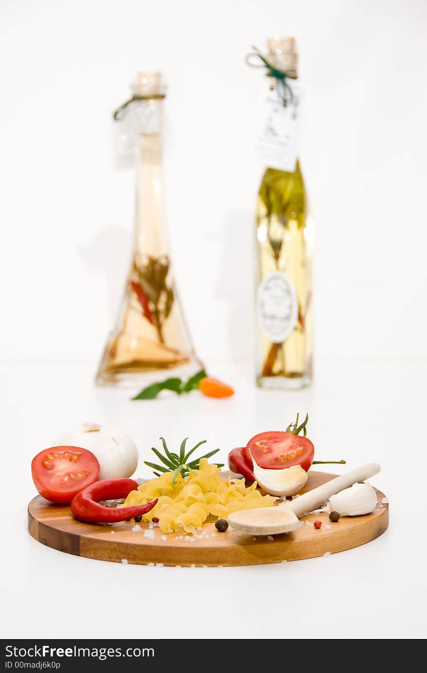 A wooden plate with tomatoes, pasta, garlic and spices in front of a vinegar- and oilbottle. A wooden plate with tomatoes, pasta, garlic and spices in front of a vinegar- and oilbottle