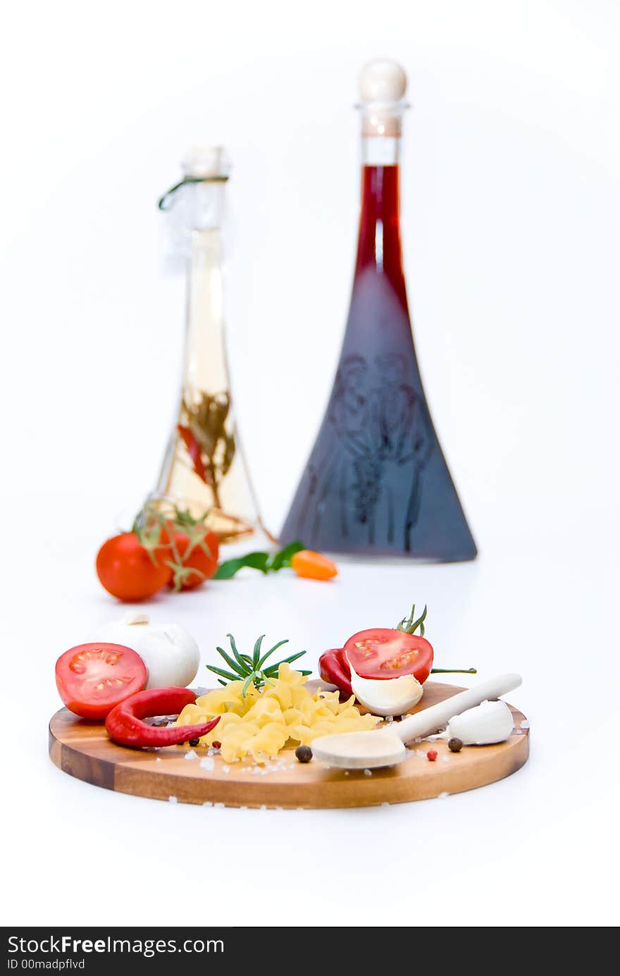 A wooden plate with tomatoes, pasta, garlic and spices in front of a vinegar and oil bottle. A wooden plate with tomatoes, pasta, garlic and spices in front of a vinegar and oil bottle