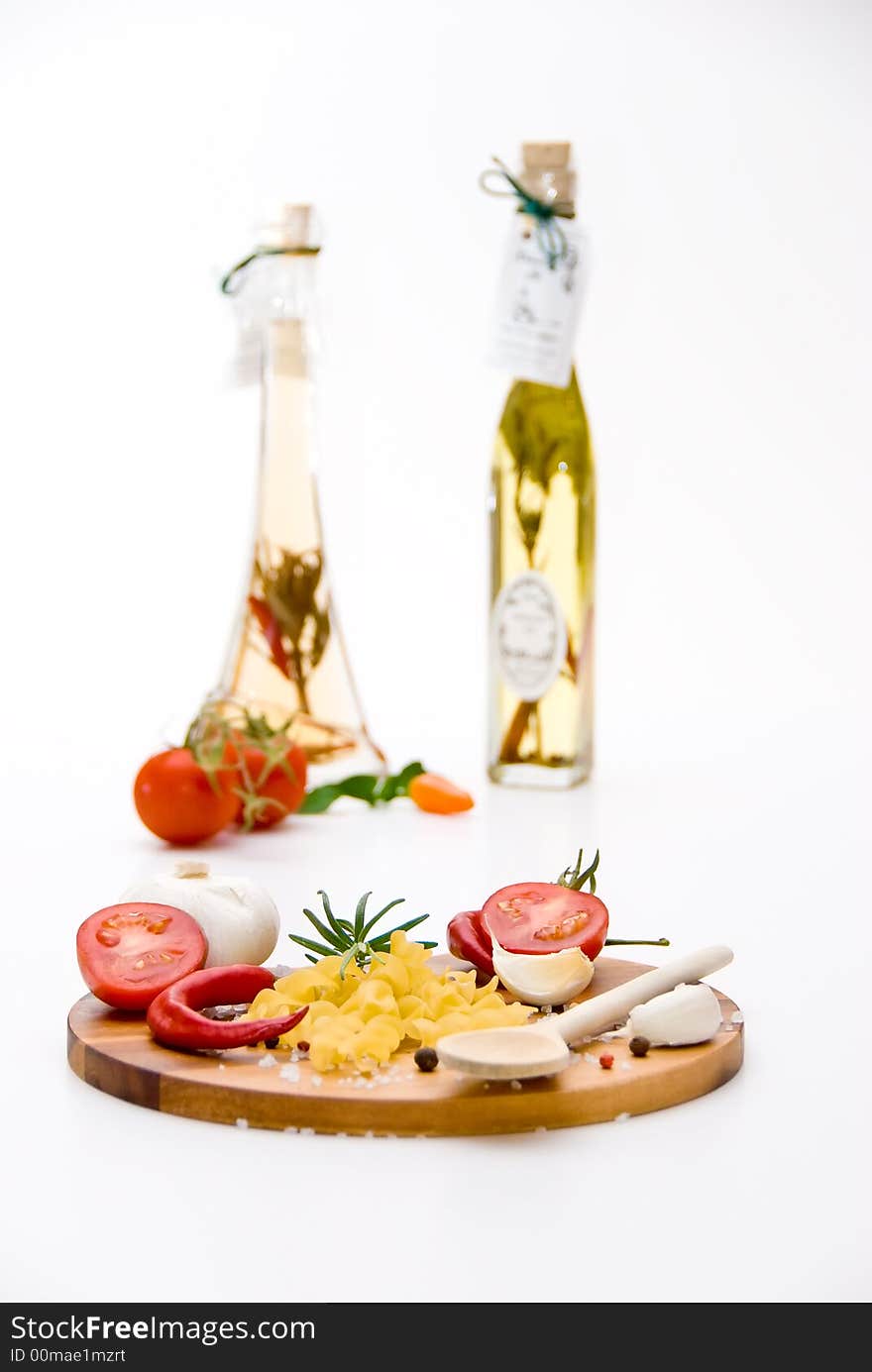 A wooden plate with tomatoes, pasta, garlic and spices in front of a vinegar- and oilbottle. A wooden plate with tomatoes, pasta, garlic and spices in front of a vinegar- and oilbottle