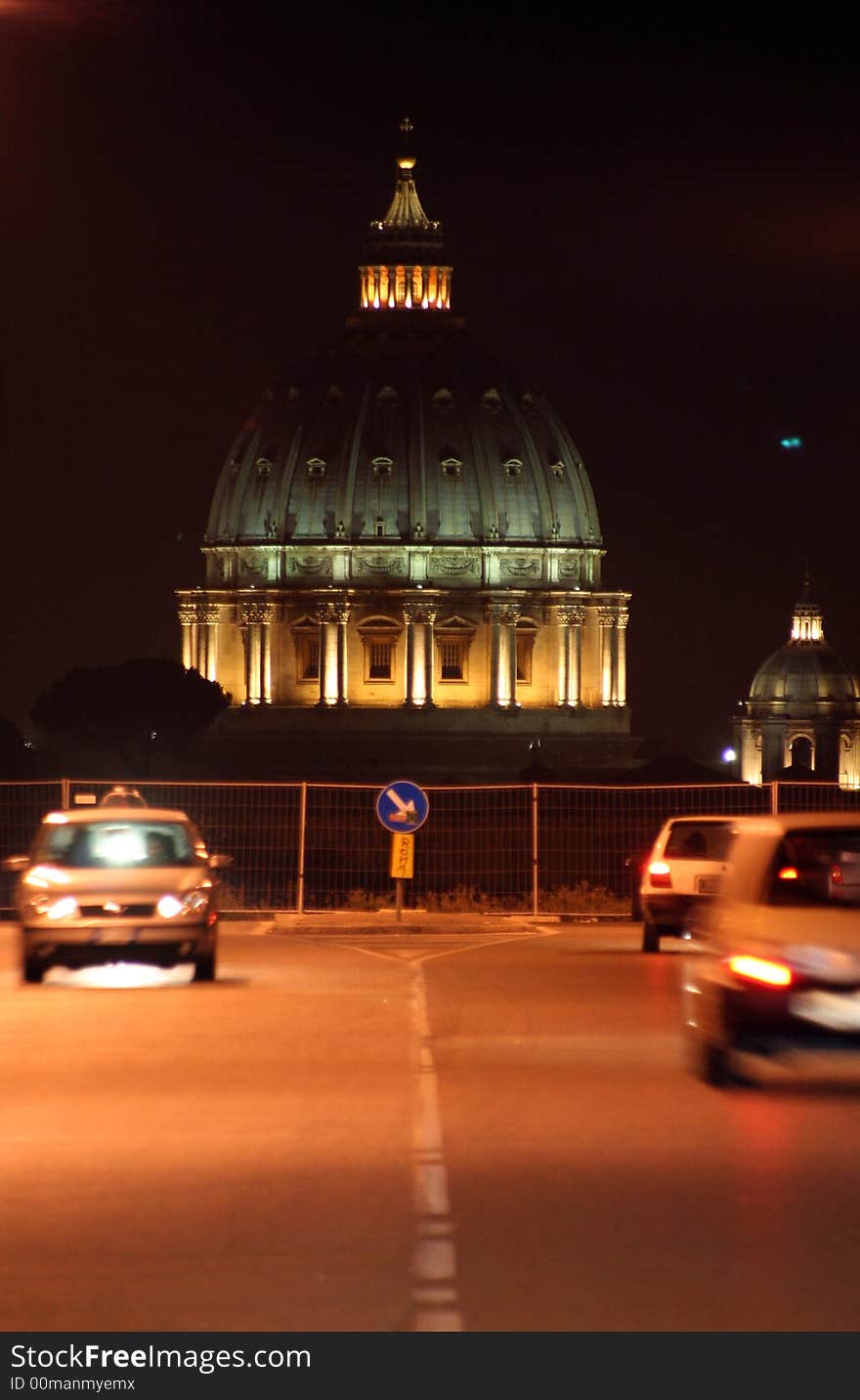 St. Peter's (Rome - Italy - Vatican City) Basilica at night / Evocative lights on the Dome / View from a urban road with vehicles movement / Signal road with arrow right. St. Peter's (Rome - Italy - Vatican City) Basilica at night / Evocative lights on the Dome / View from a urban road with vehicles movement / Signal road with arrow right