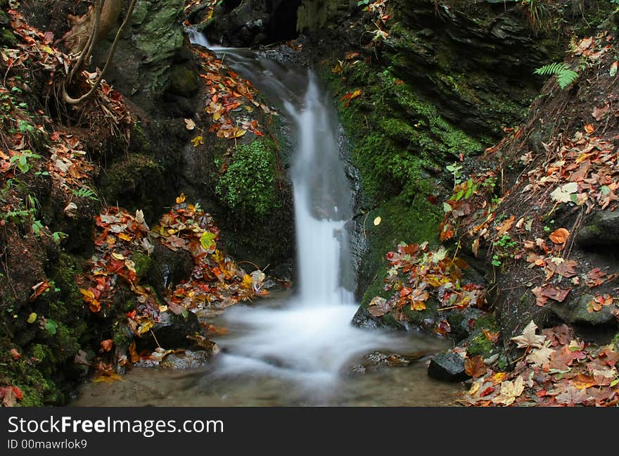 Small waterfall surrounded by autumn colored leaves and green moss. Small waterfall surrounded by autumn colored leaves and green moss