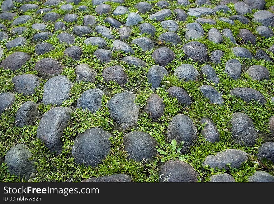 A close up of a typical medieval paving in Bologna - Italy - with grass and pebbles. Cobbled paving. A close up of a typical medieval paving in Bologna - Italy - with grass and pebbles. Cobbled paving.