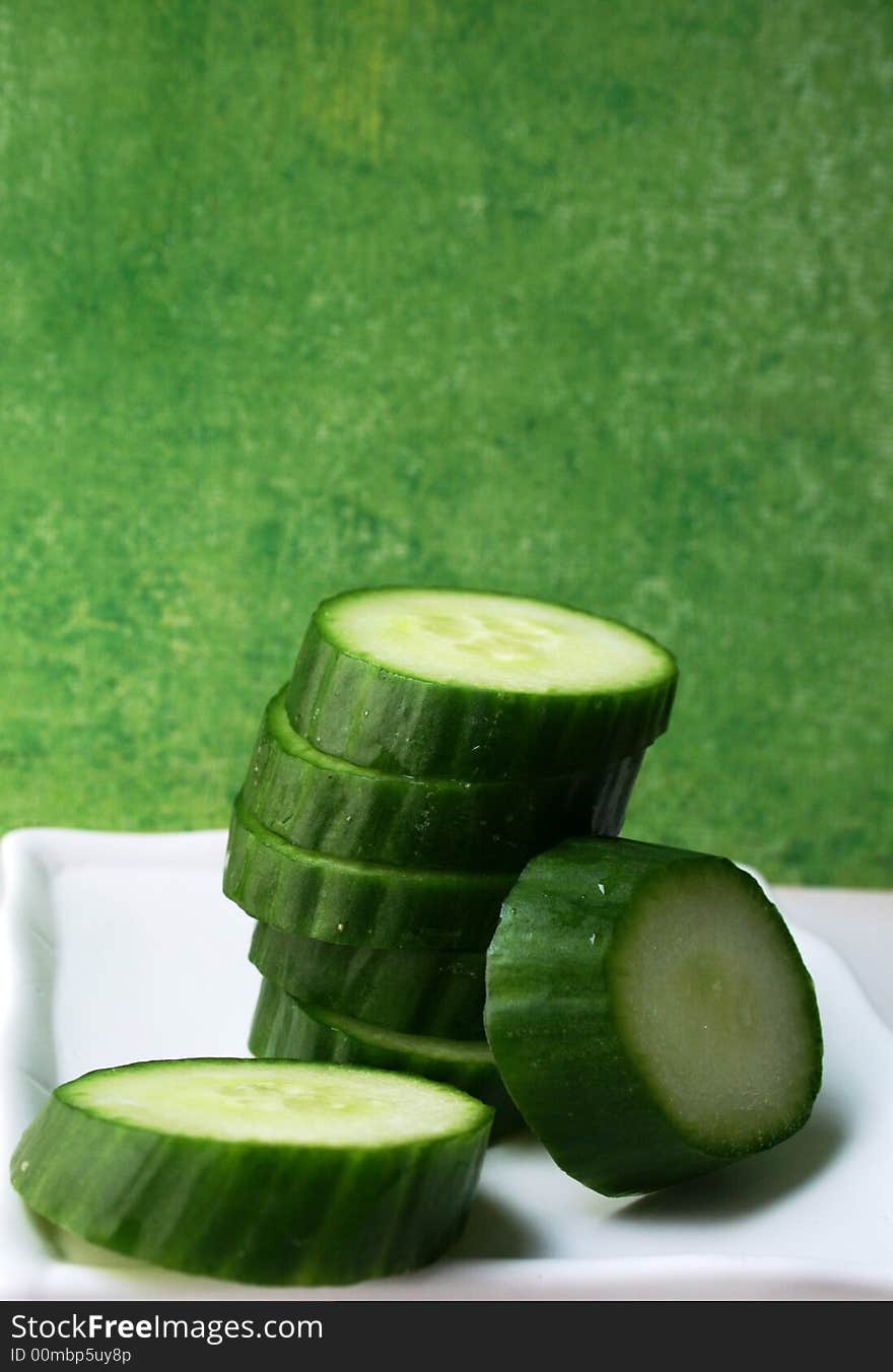 Sliced cucumber on white plate with green background