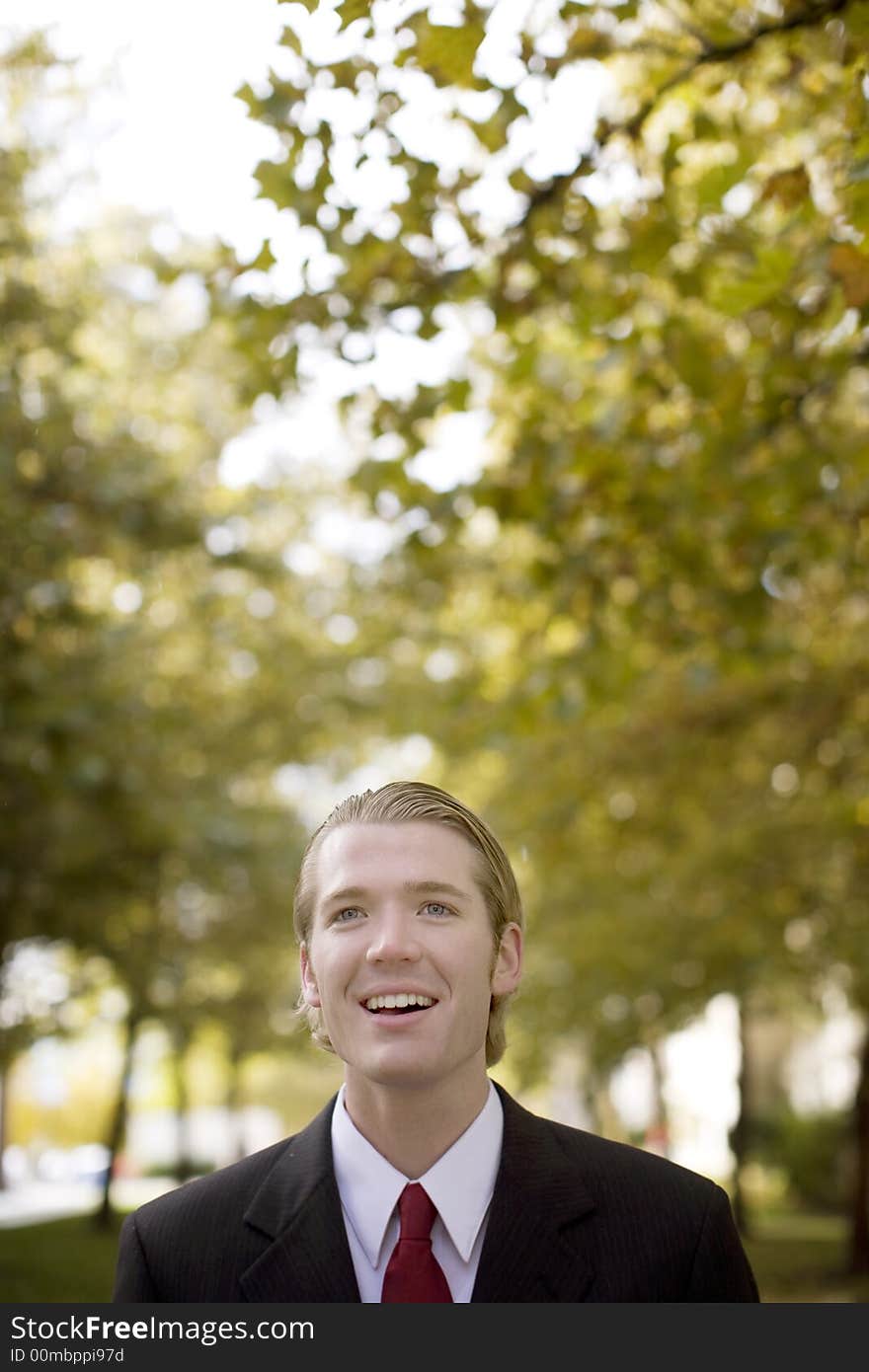 One businessman looking past camera with open mouth dressed in business full suit with red tie and trees in background. One businessman looking past camera with open mouth dressed in business full suit with red tie and trees in background