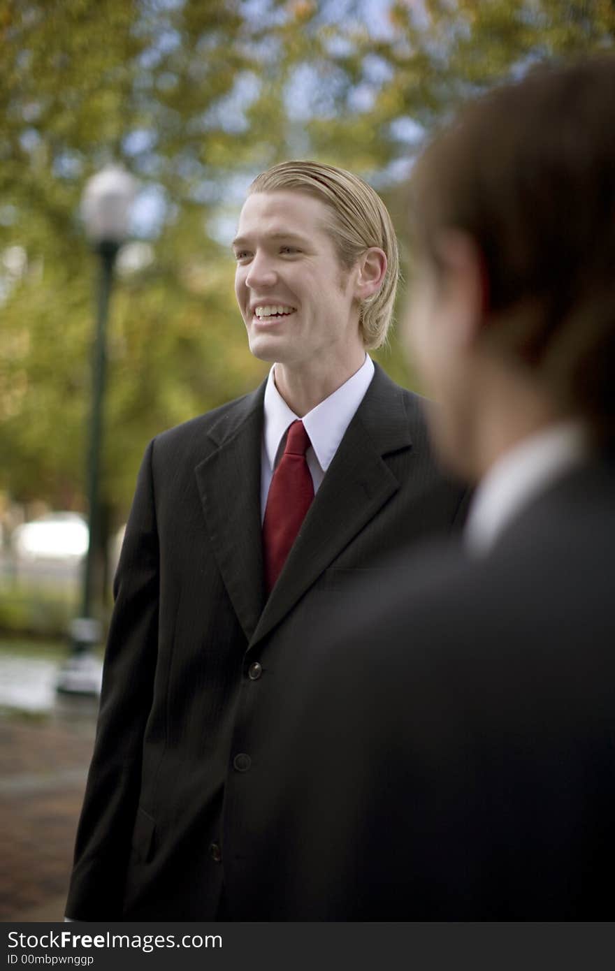 Over the shoulder waist-up shot of two businessmen one is laughing. Over the shoulder waist-up shot of two businessmen one is laughing